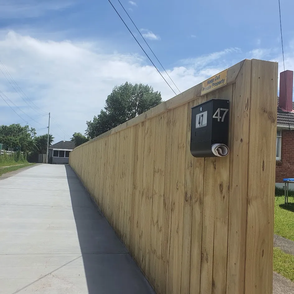 Newly poured textured concrete driveway next to a wooden fence and gravel area.
